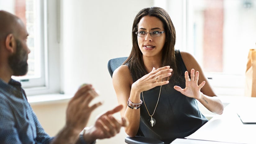 People in office having a discussion at desks by big windows